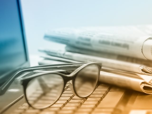 A pair of glasses resting on top of a laptop computer near a newspaper.
