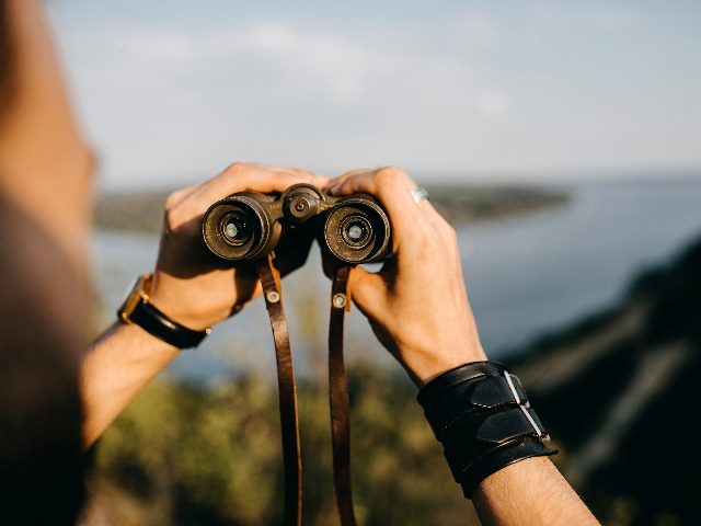 Close-up of a man holding binoculars in mountains. 