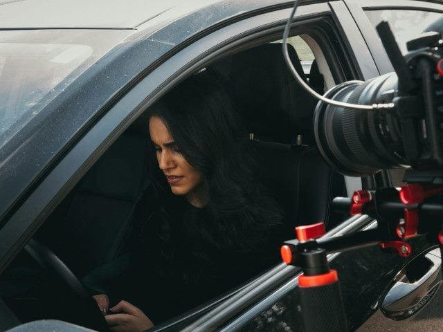 An actor in a car being filmed by a camera.