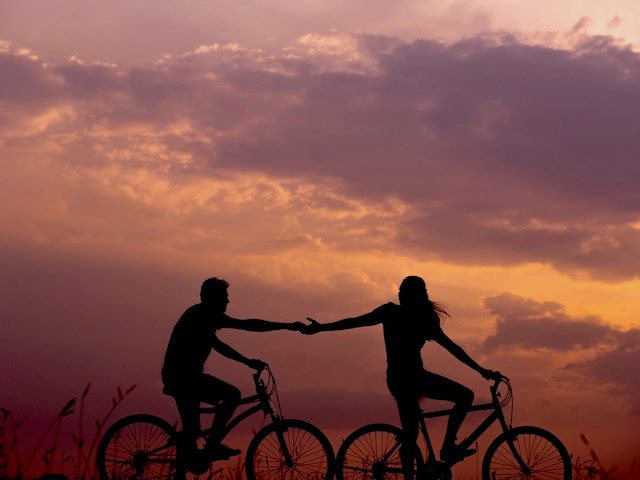 humans holding hands while biking