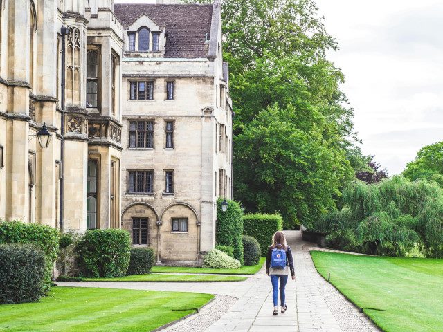 A student walks on a path beside buildings on a college campus.