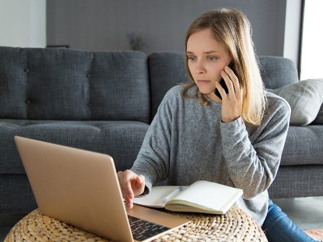 Woman sitting down, talking on the phone and looking at a laptop.