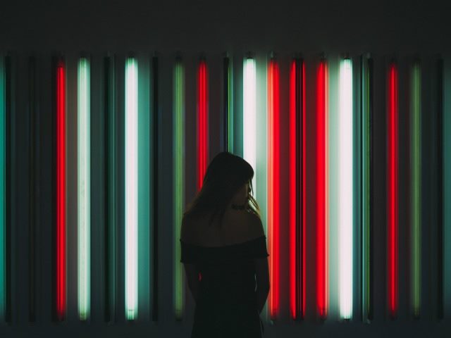 looking over shoulder in front of neon sign