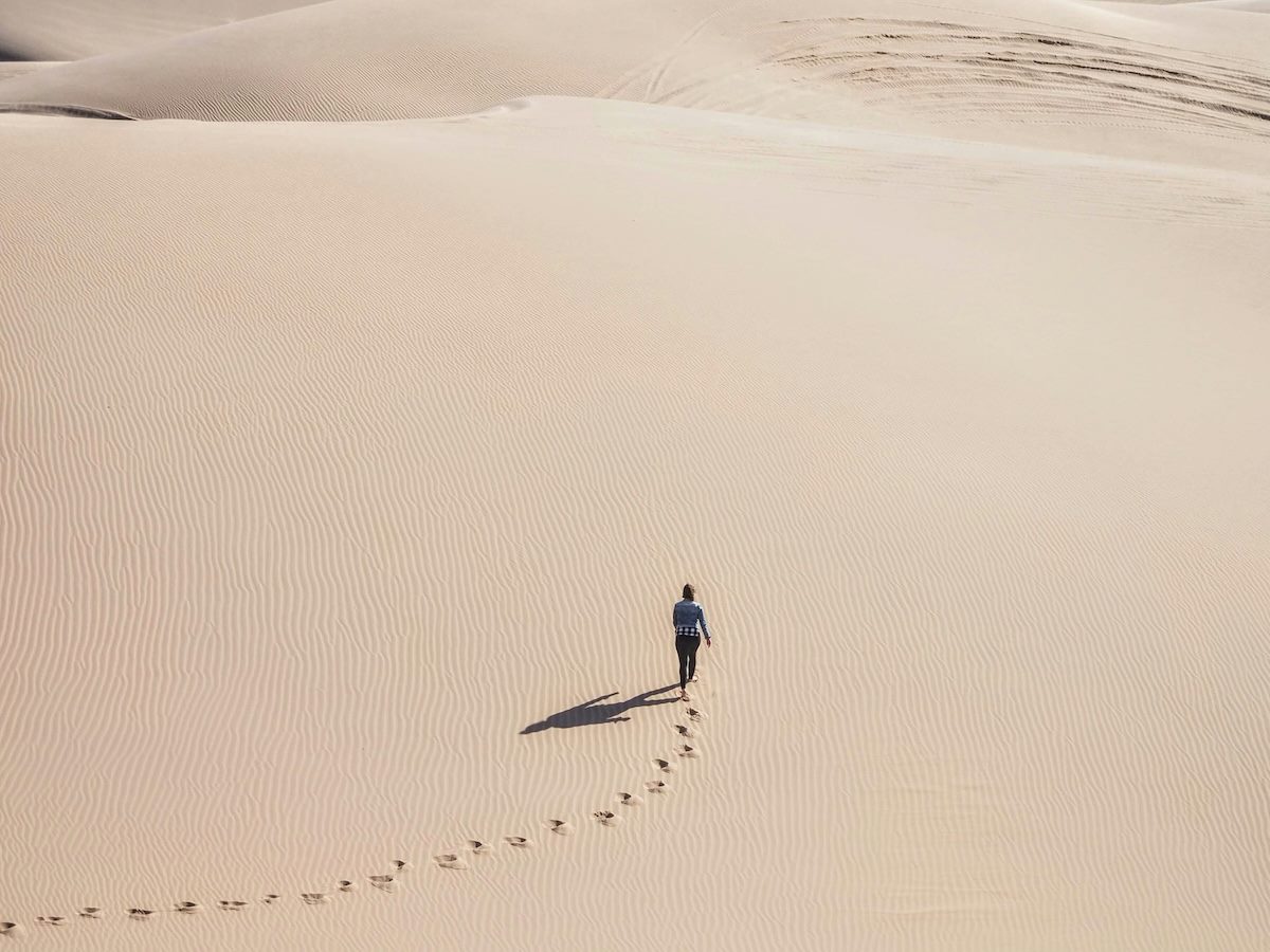 person walking away from the camera in a dessert, leaving a trail of footprints behind them