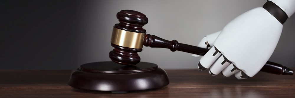 A white robot hand holds a gavel above a sound block sitting on a wooden table.