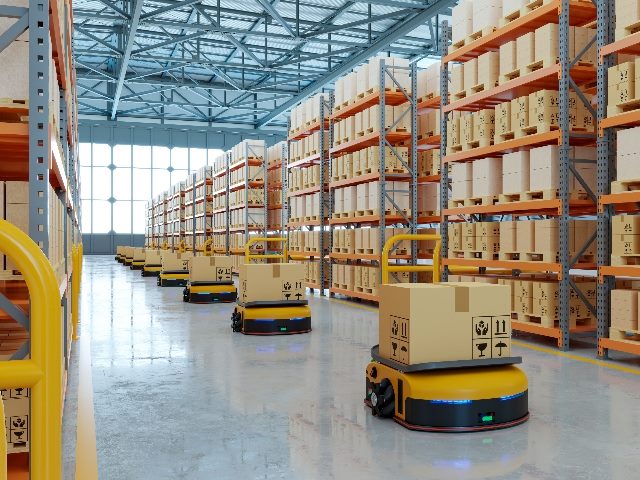 AGVs (Automated guided vehicles) on warehouse floor surrounded large stacks of boxes. 