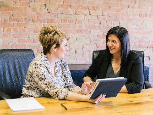 Two employees look at a computer tablet at a conference table.