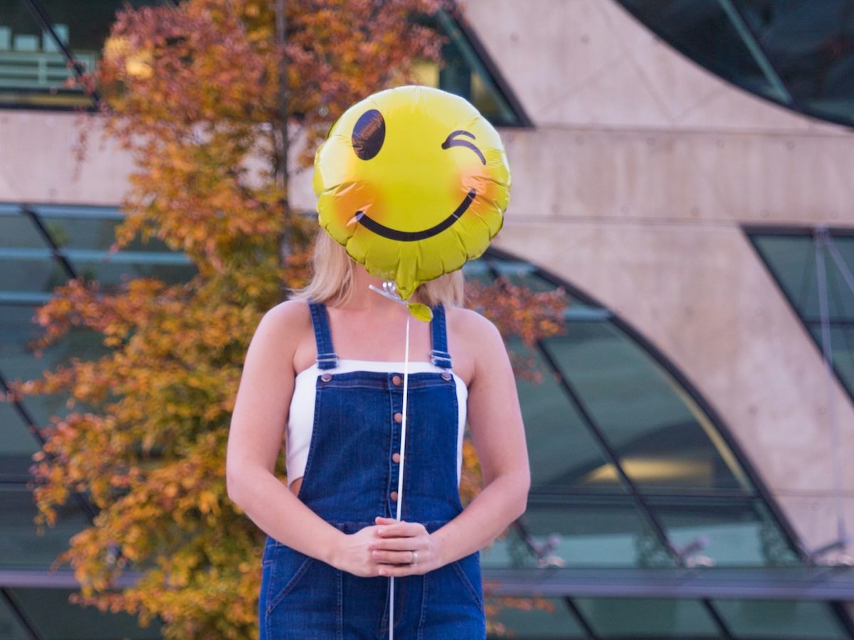 woman holding a balloon with a winky emoji face  in front of her face 