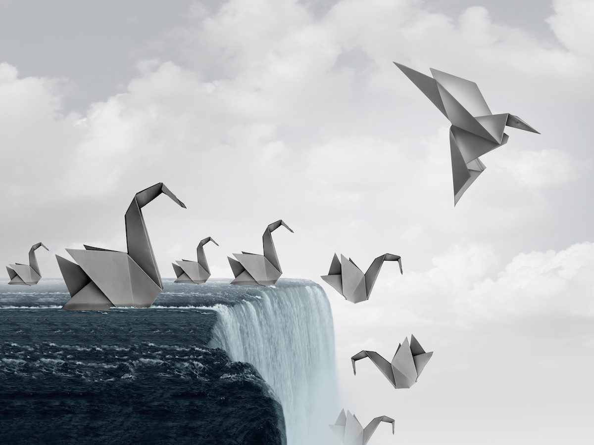 Adapt to survive concept as paper swans falling off a waterfall and one origami bird adapting new skills and flying away to safety