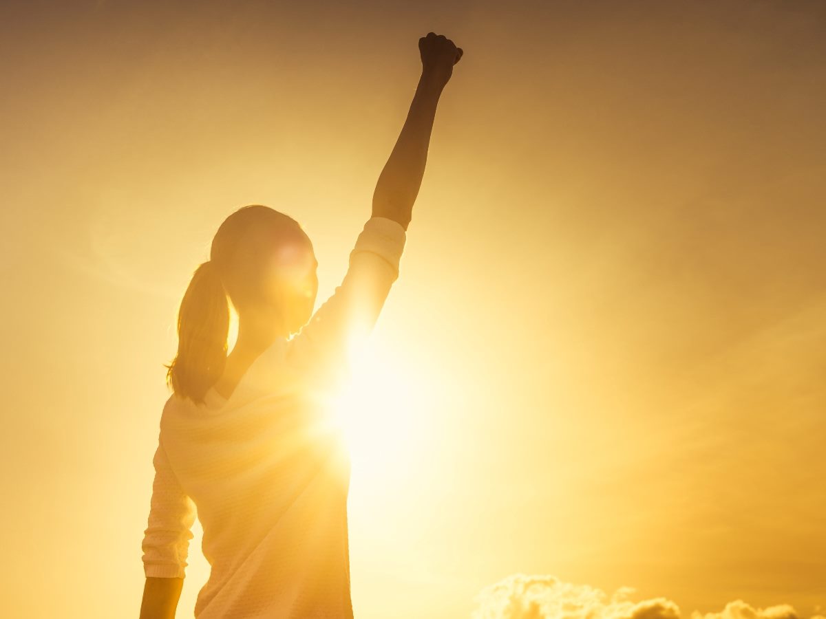 Woman holding arm up in confidence with the sun shining down.