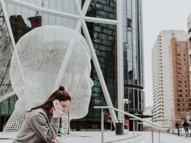 woman sitting in front of an outdoor sculpture speaking on the phone