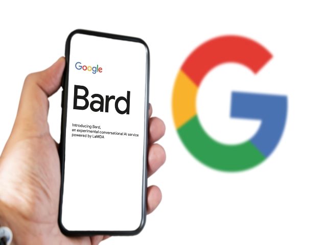 A hand hold a cell phone with the search Bard on the screen. Google appears in the background.
