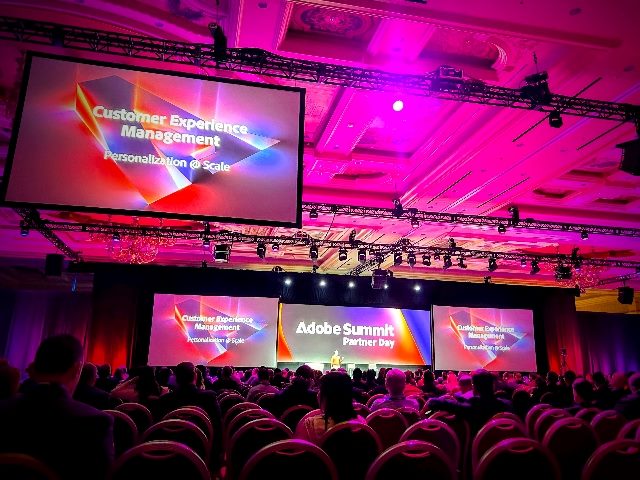 Adobe Summit 2024 Partner Day at the Venetian Hotel in Las Vegas. A shot of the crowd, a sign with Adobe label hanging from the ceiling and a large screen onstage with more Adobe labels.