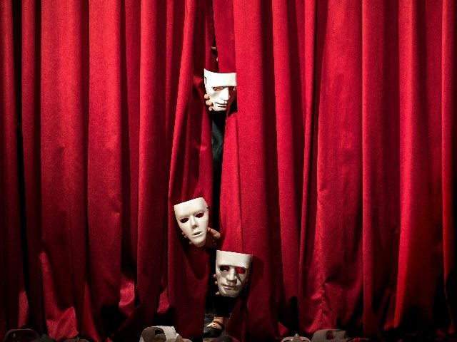 Red velvet curtains hang before a theater stage with three white masks placed on the curtains, suggesting the similarity of customer experience strategy to theater performance. 