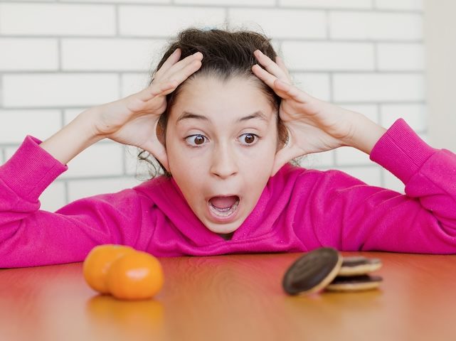 Girl struggling to make a hard decision between fruits and cookies