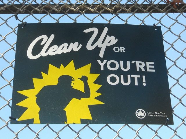 sign on a fence that says, "Clean up or you're out!"