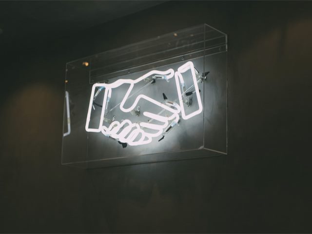A white neon sign in the shape of a handshake icon