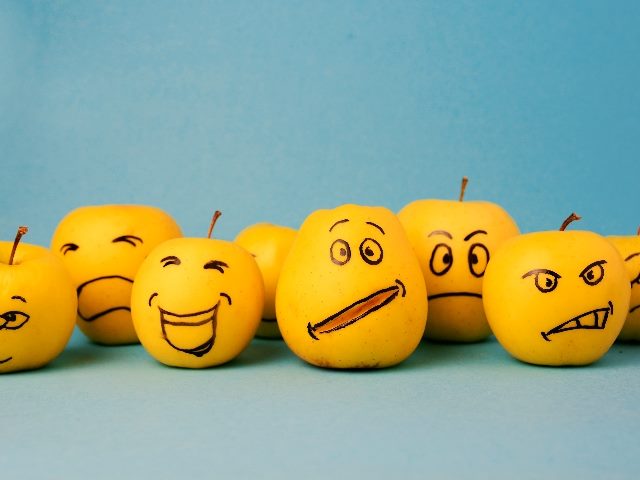 Different emotions from joy to sadness and anger on faces drawn on yellow apples in piece about sentiment analysis and voice of the customer data. 