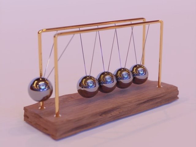 Wooden Newton's Cradle against a light mauve background