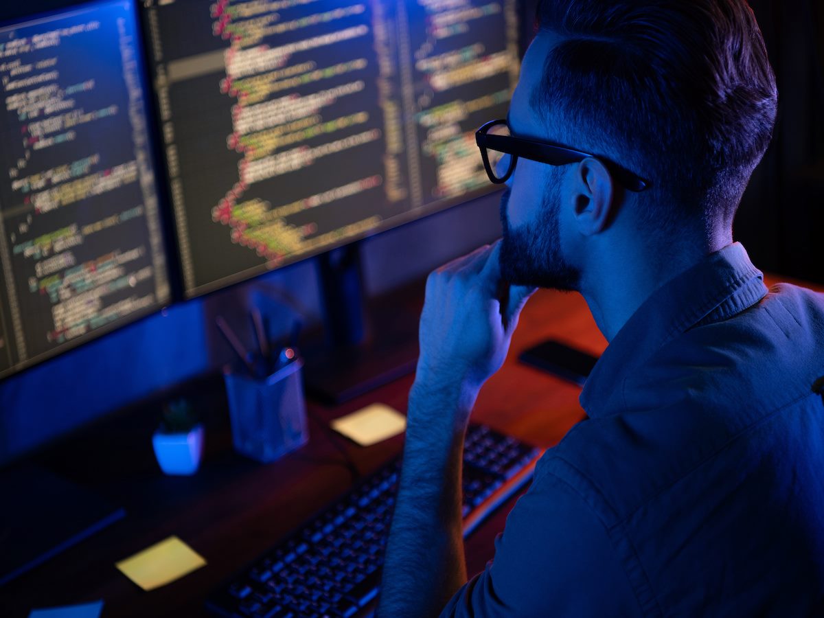 A person looking at computer monitors with code 