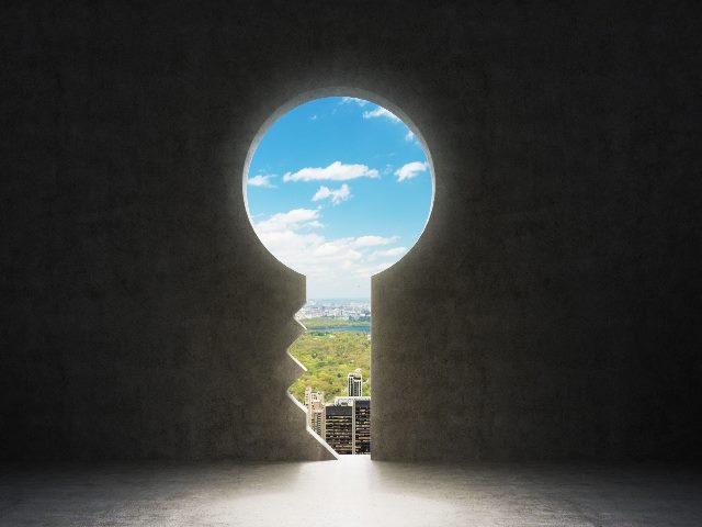 A keyhole in the concrete wall reveals a view New York City with blue sky and white clouds, symbolizing the omnichannel customer journey of the future. 