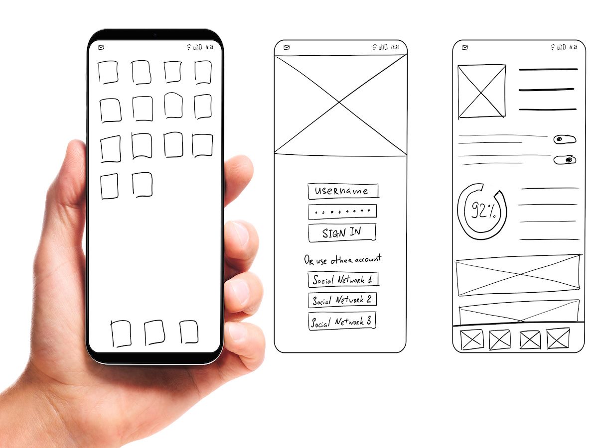 hand holding smartphone with wireframed user interface screen prototypes of a mobile application