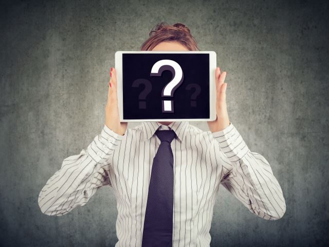 A woman in business attire holding a tablet with a question mark on the screen over her face