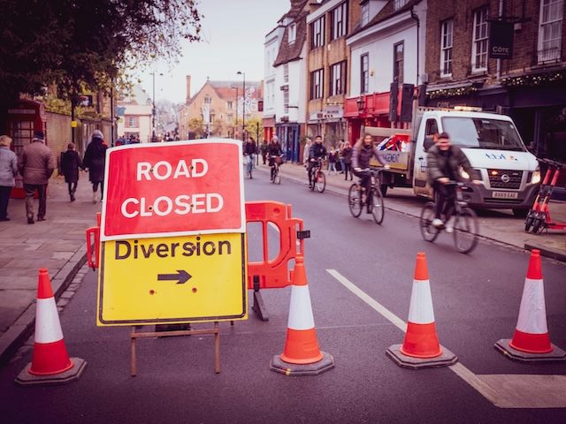 road closed, diversion sign on road in the UK. pedestrians and bicyclists in the background