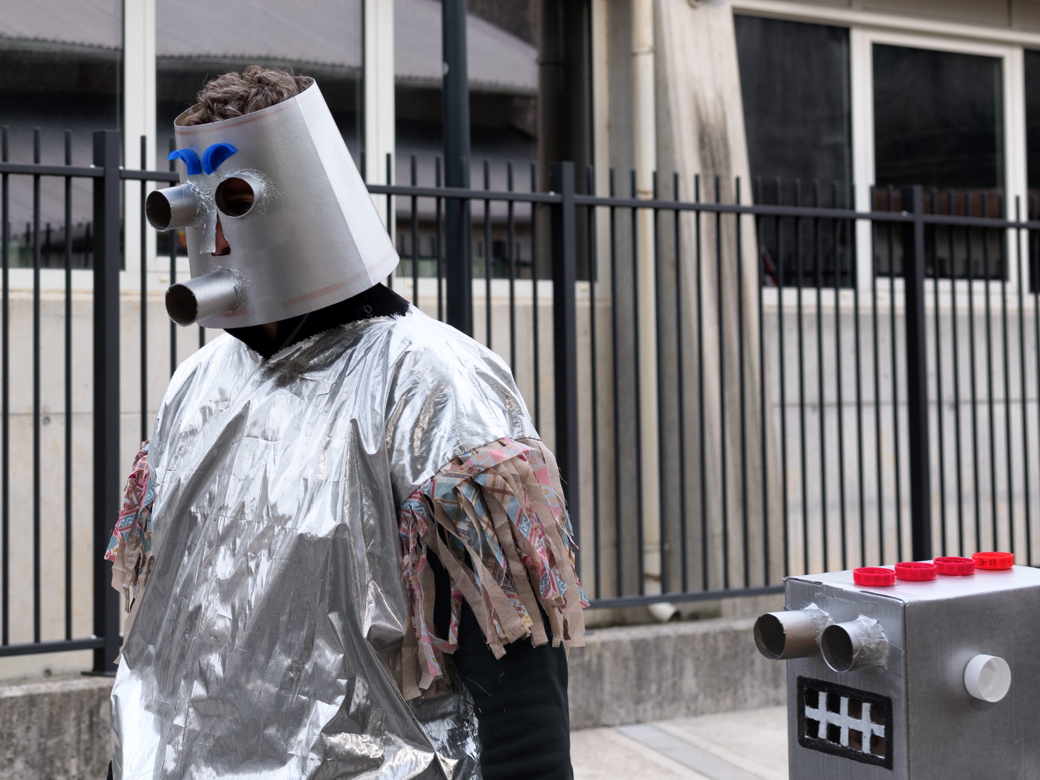 Two vintage silver robot-costumed people walking in the street.  