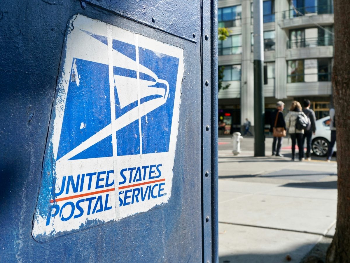Close-up view of USPS mailbox with people in the background.
