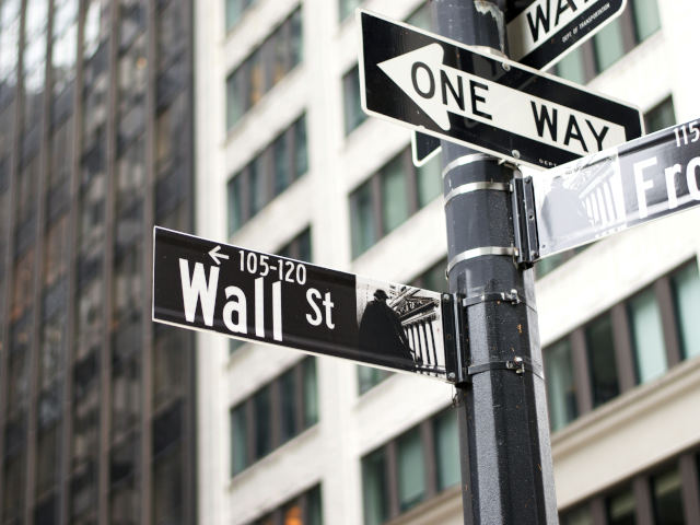 A Wall St sign and one way sign hang on a street pole in New York City.