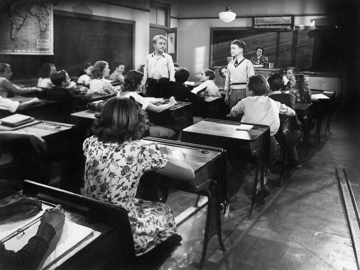 Children in a class room with a teacher and two boys looking at each other