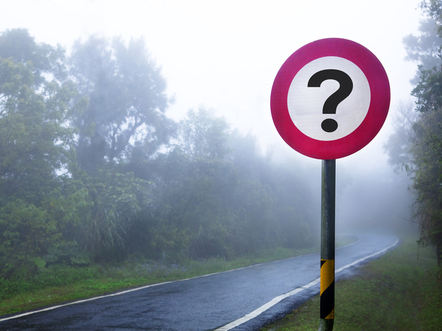 A road sign with a question mark on it, on a foggy road. - question concept