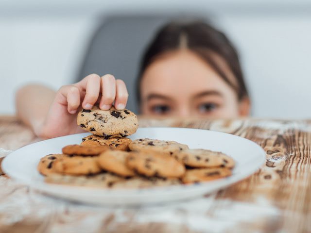 little girl stealing a cookie off a full plate