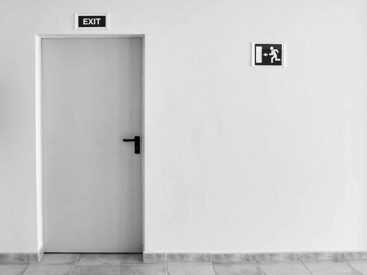 minimalist photo with a door, an exit sign, and another sign showing a figure running for the exit