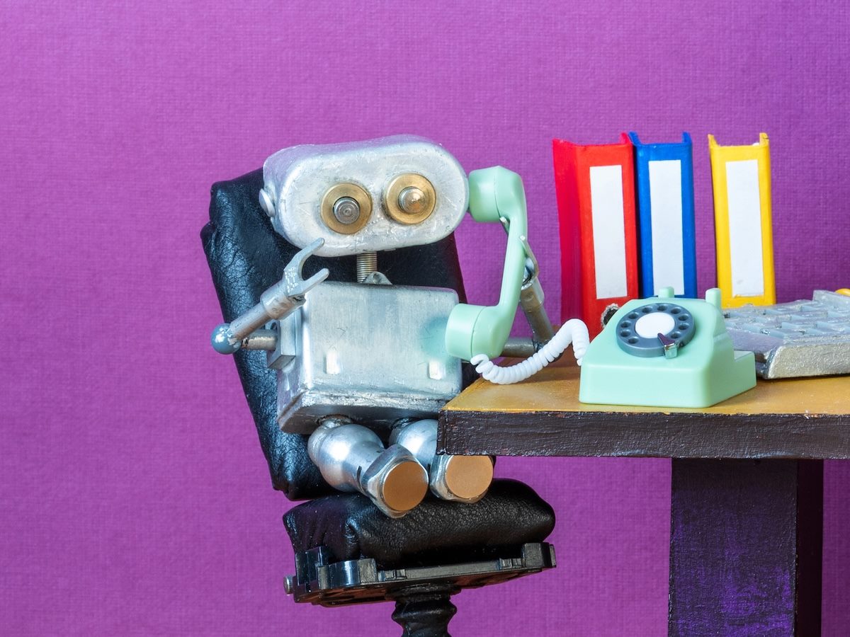 Close-up of silver metal toy robot hotline operator sitting relaxed at office desk in chair