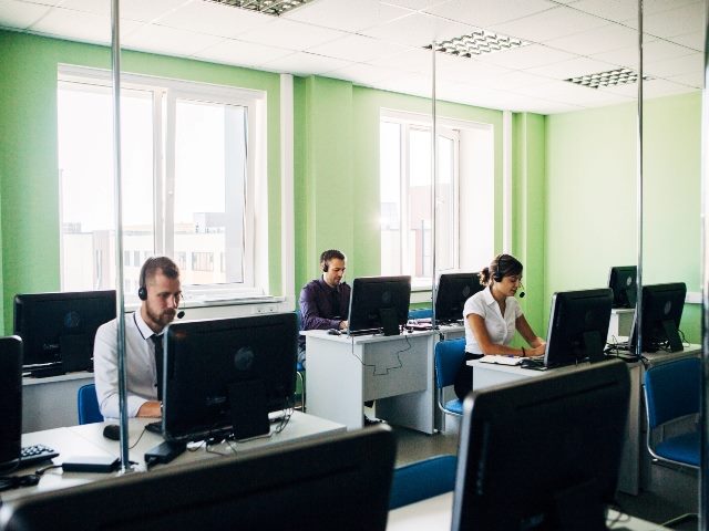 Three call center operators at work behind a glass.