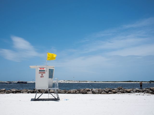 unattended beach with an empty lifeguard seat, yellow flag flying