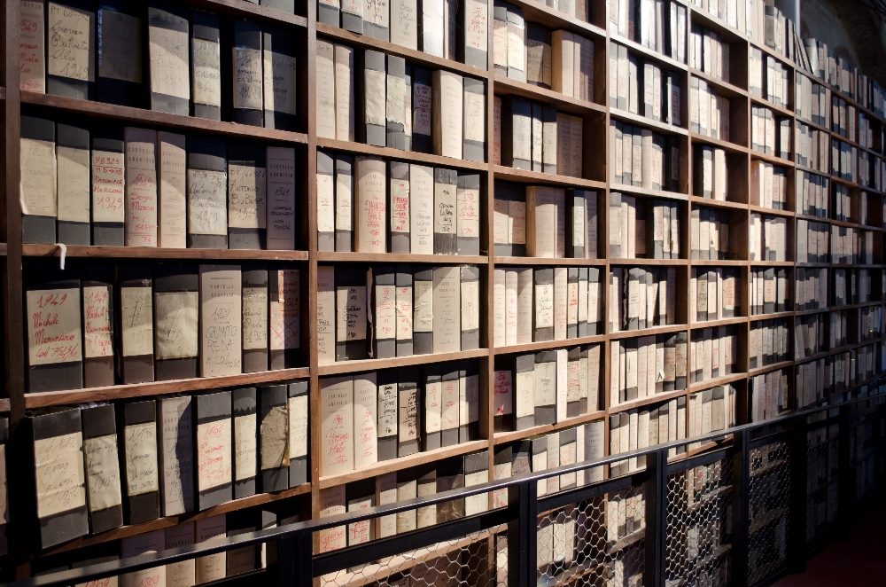 A library archive with numerous shelves filled with organized, labeled boxes and binders, showcasing a system of meticulous record-keeping and storage. The labels display handwritten notes and dates, indicating a historical collection in piece about the evolution of AI in DAM (digital asset management).