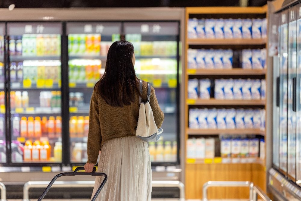 A woman stands in a grocery store contemplating possible purchases as she gazes at products, indicating the impact of AI on the customer journey.