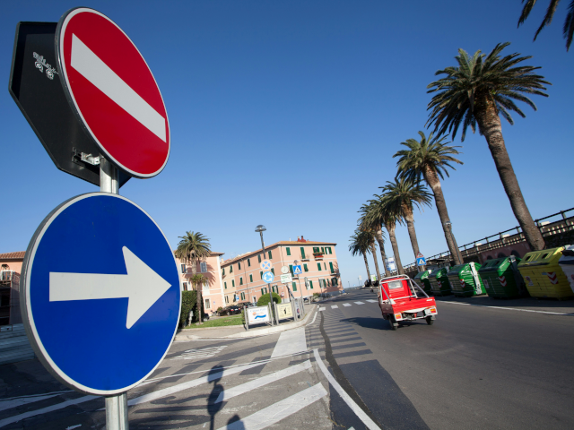 A right turn sign and a stop sign stand beside a road with palm trees.