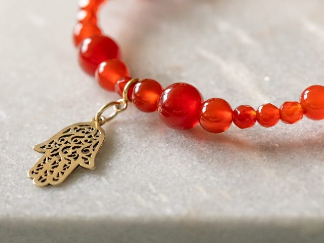 Red bracelet made out of carnelian stone with a hamsa charm. 