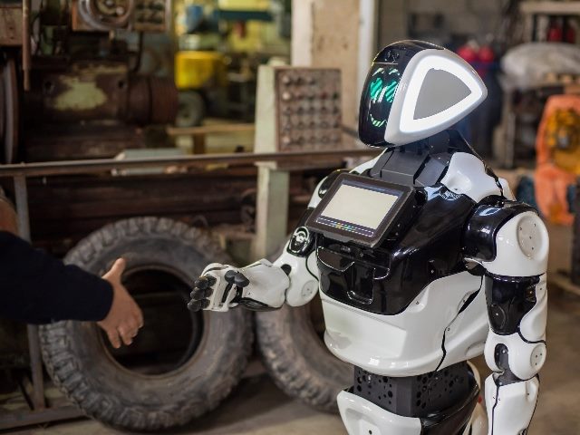 Humanoid robot on wheels with a monitor on his chest, shaking hands with a man.  
