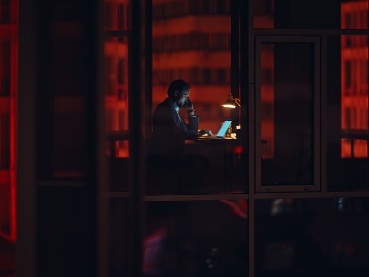 Night businessman silhouette window working alone at night talking smartphone