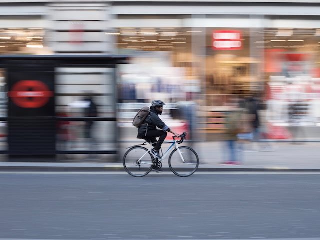 time lapse photo of bicyclist, bundled up against cold weather, riding down the street