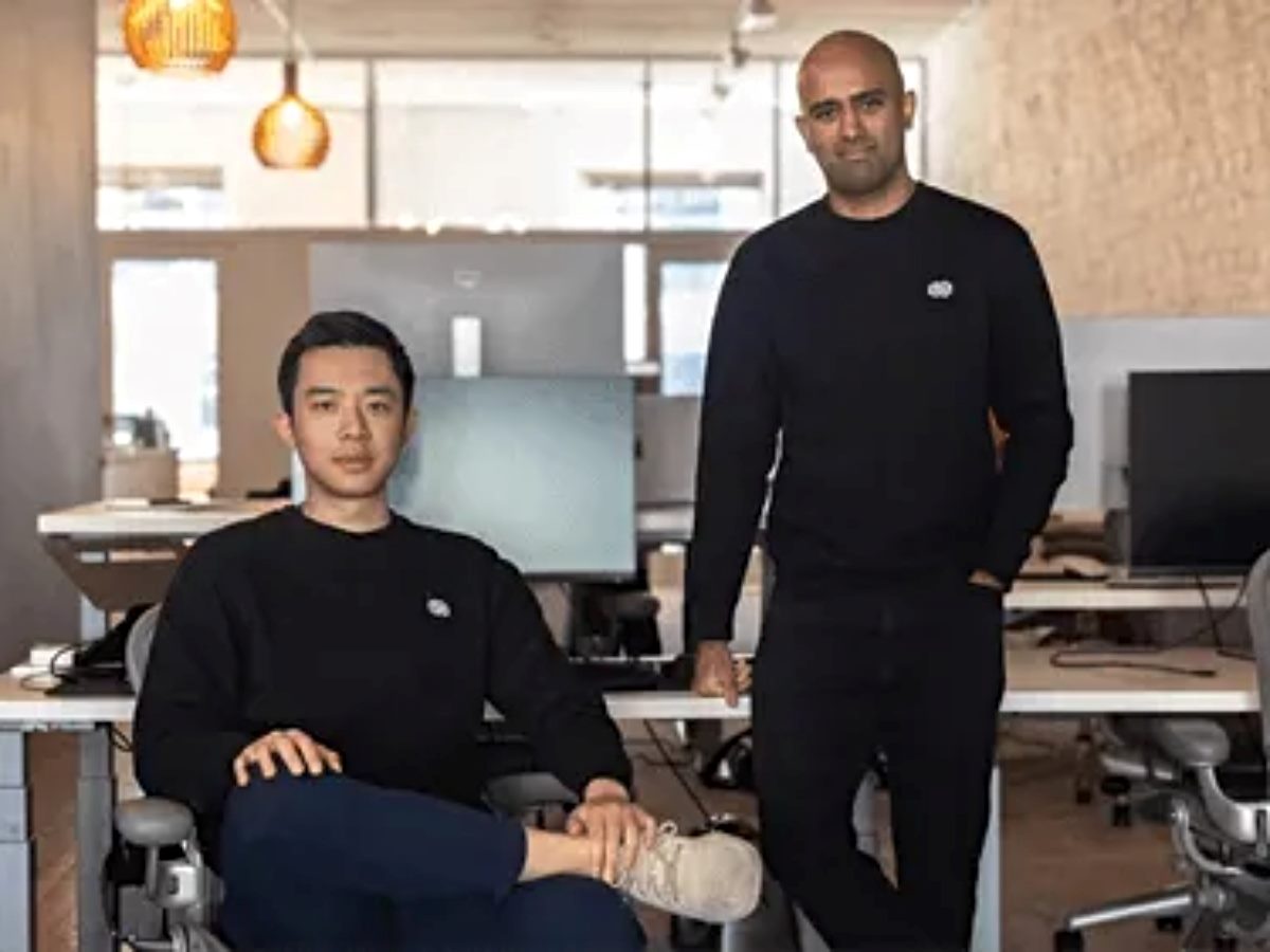 Decagon co-founders Jesse Zhang (left), CEO, seated at a desk, and Ashwin Sreenivas, president, standing beside him in a modern office workspace.