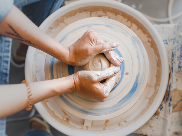 An overhead view of hands with clay making of a ceramic pot on the pottery wheel