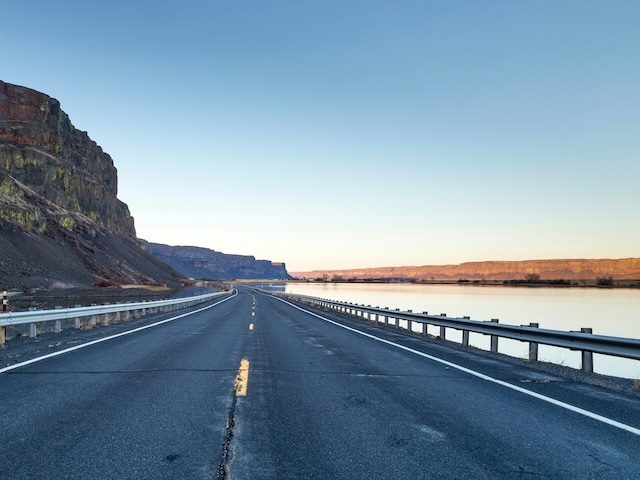 an empty highway next to a river, with a set of guardrails in place