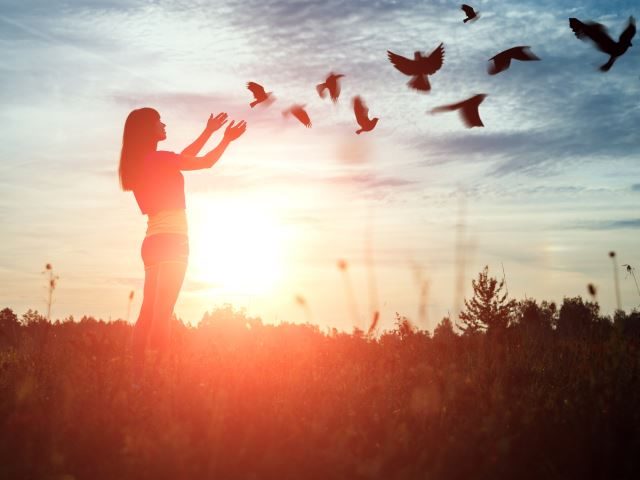 A  silhouetted young girl liberating a flock of birds 