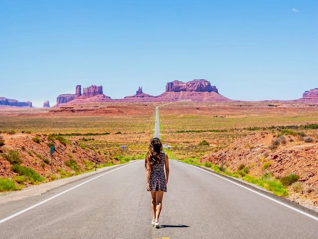 woman walking towards monument valley on a long, deserted  road